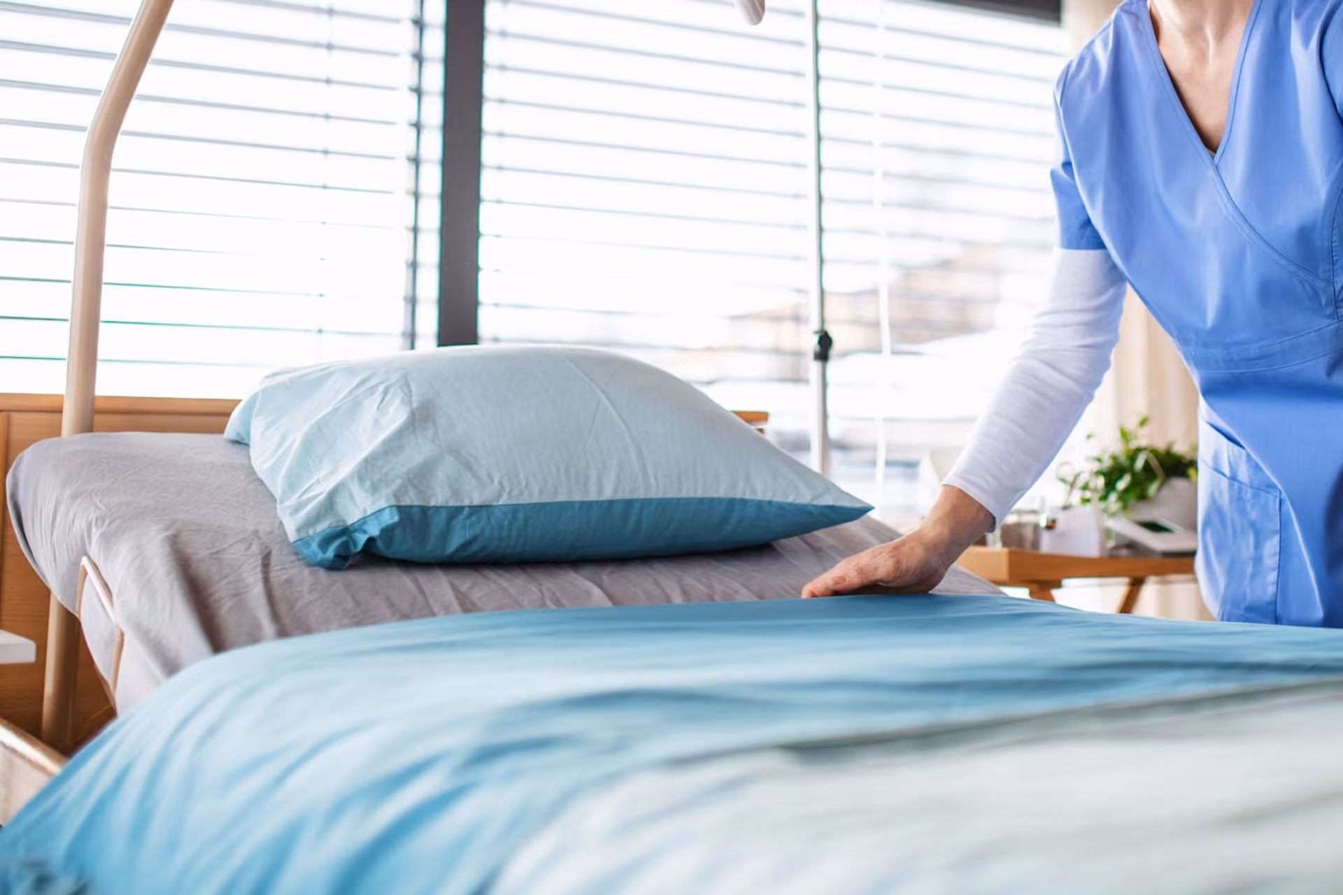 Pflegekraft richtet ein Klinikbett mit hellblauer Bettwäsche
